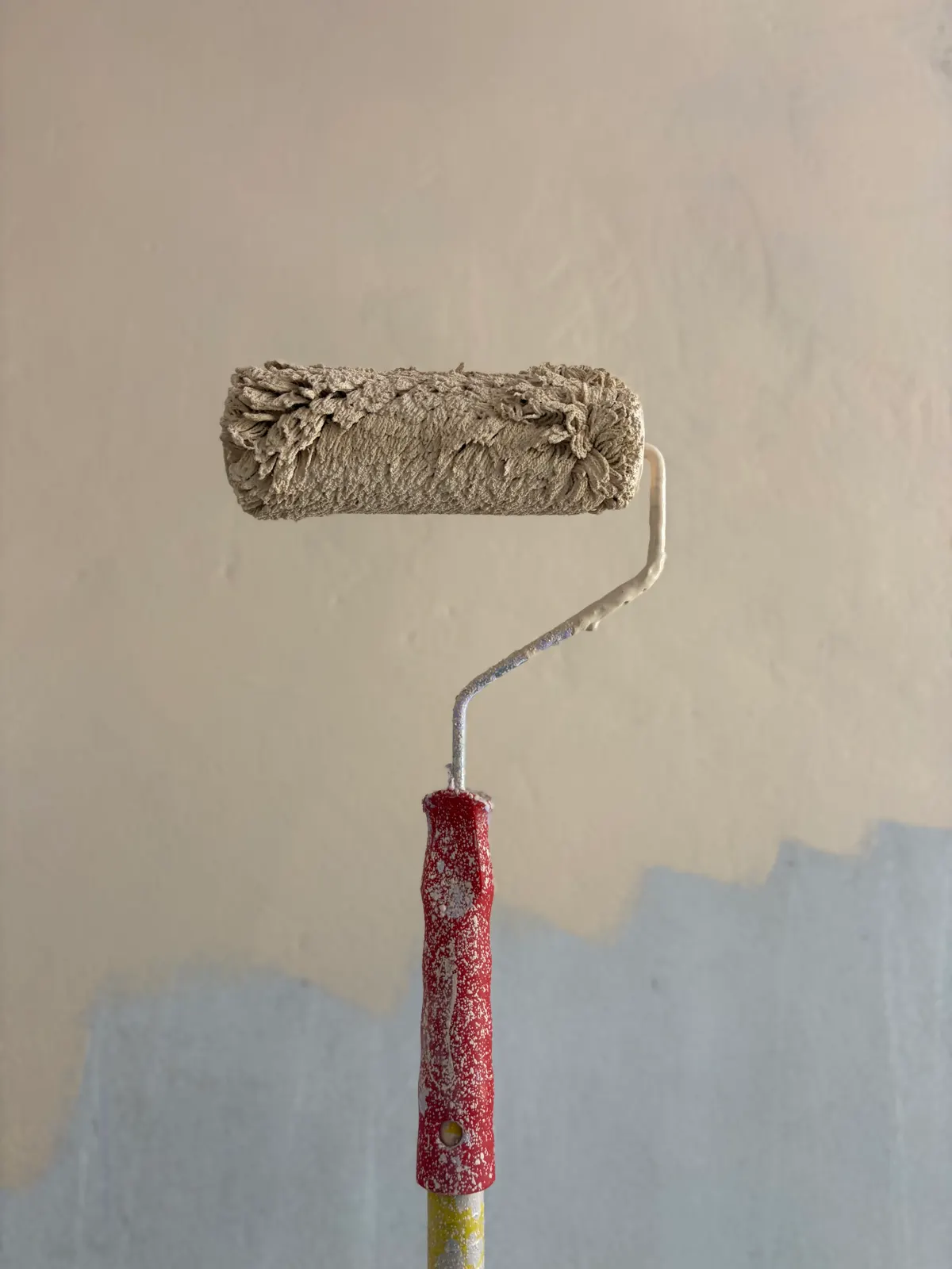 Paint roller loaded with fresh color resting against a half finished wall