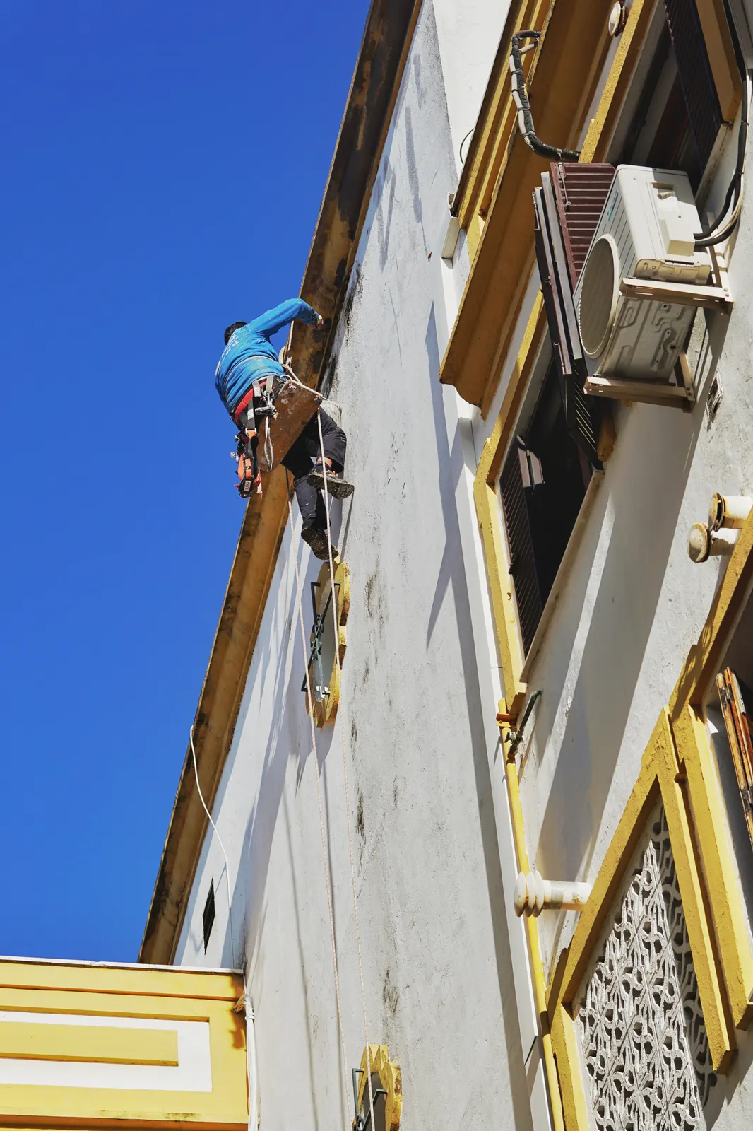 Painter working on window trim high on a building exterior